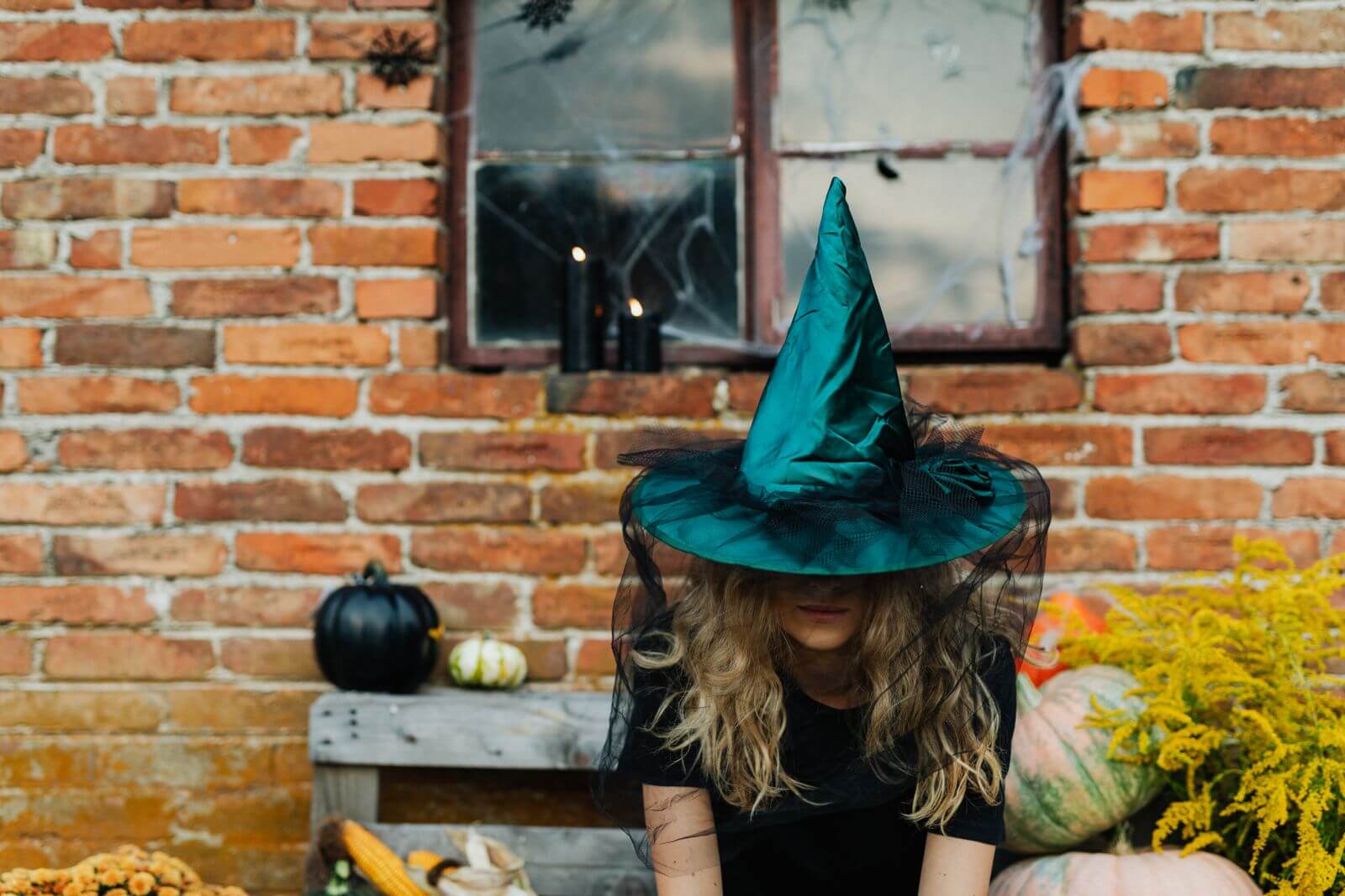 Woman in a witch hat and costume sitting beside pumpkins